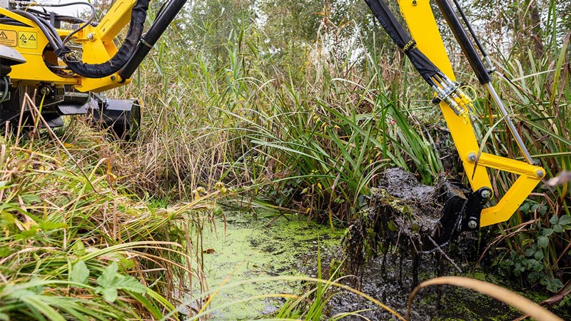 A Truxor Machine Using a Yellow Excavator Arm to Scoop Out Dense Sediment
